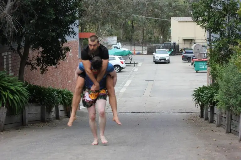 man performing a piggyback carry as part of outdoor strength training at functional fitness eltham