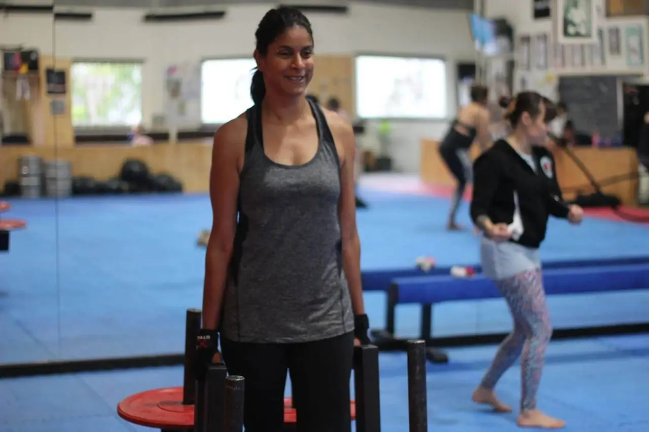 woman smiling while carrying weights during a women only fitness class at functional fitness eltham with other women exercising in the background in a supportive group environment